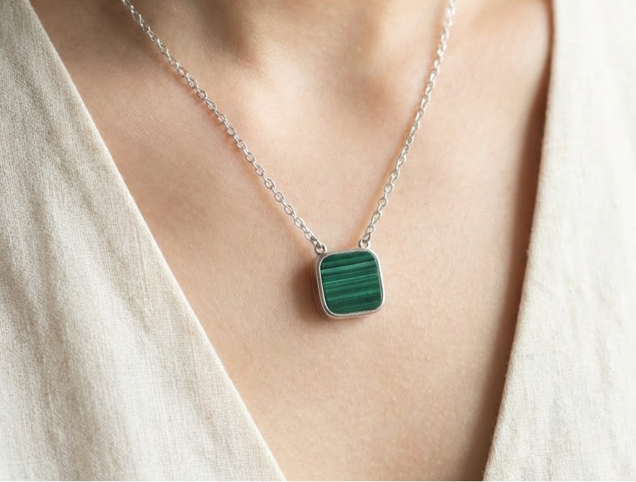 Necklace with a green malachite square pendant worn by a person in a light-colored top